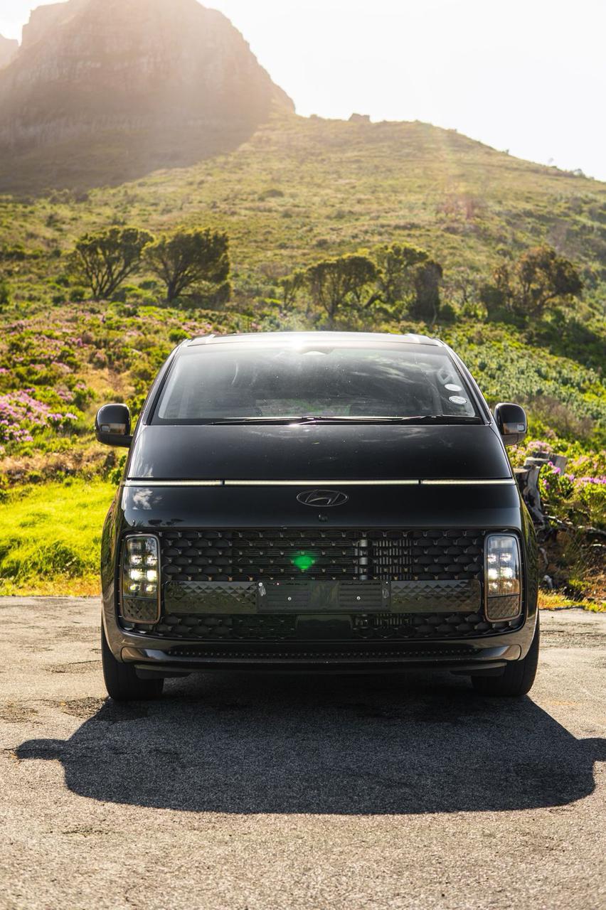 Black Hyundai Staria front view with mountain backdrop